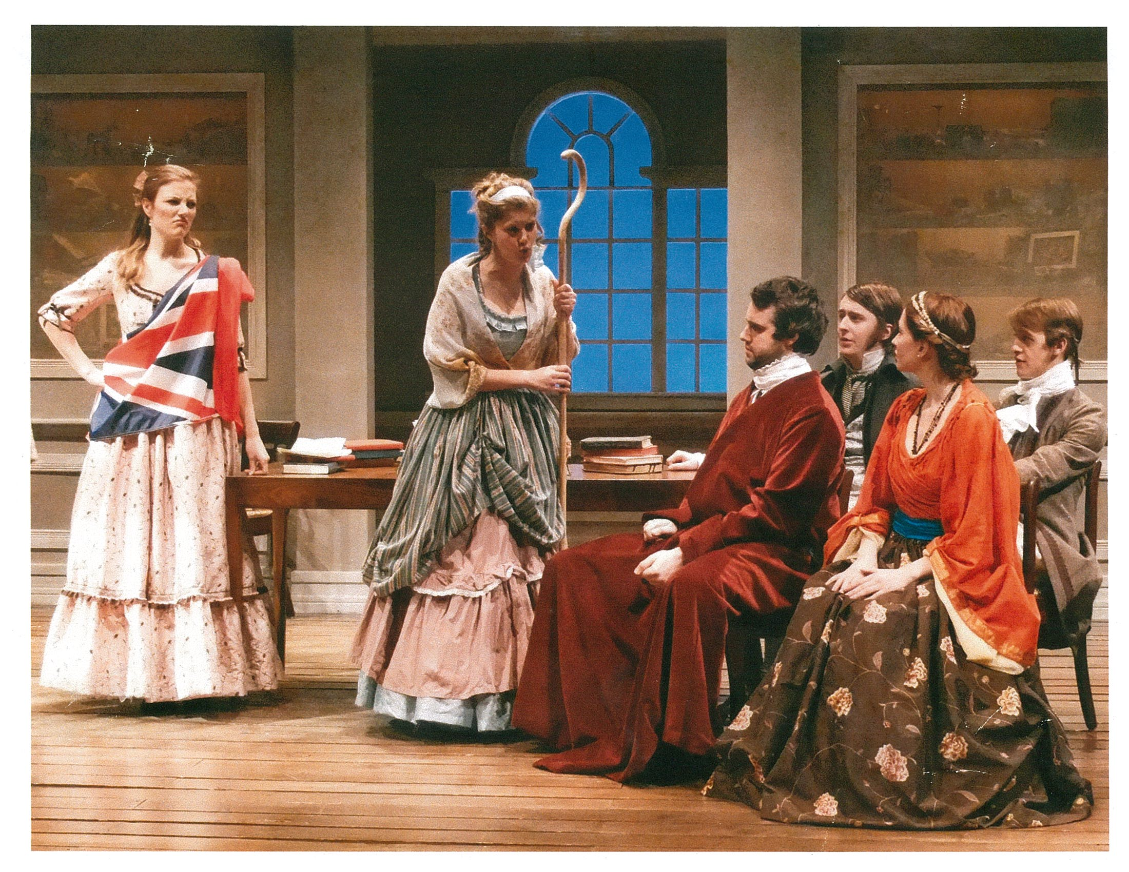 Four people sitting looking at two women standing to the left