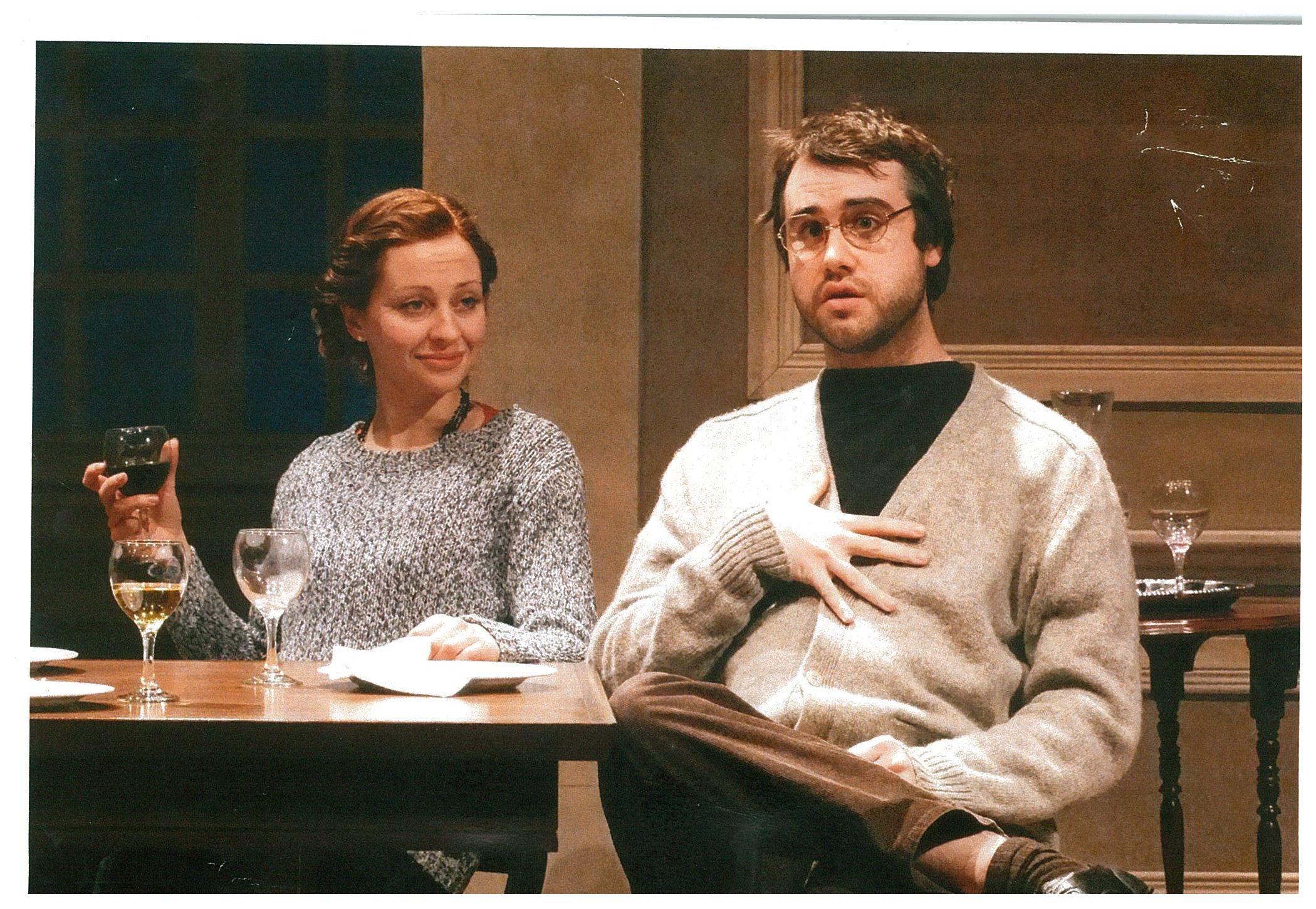 A woman sitting with a glass wine and a man speaking to someone off-screen