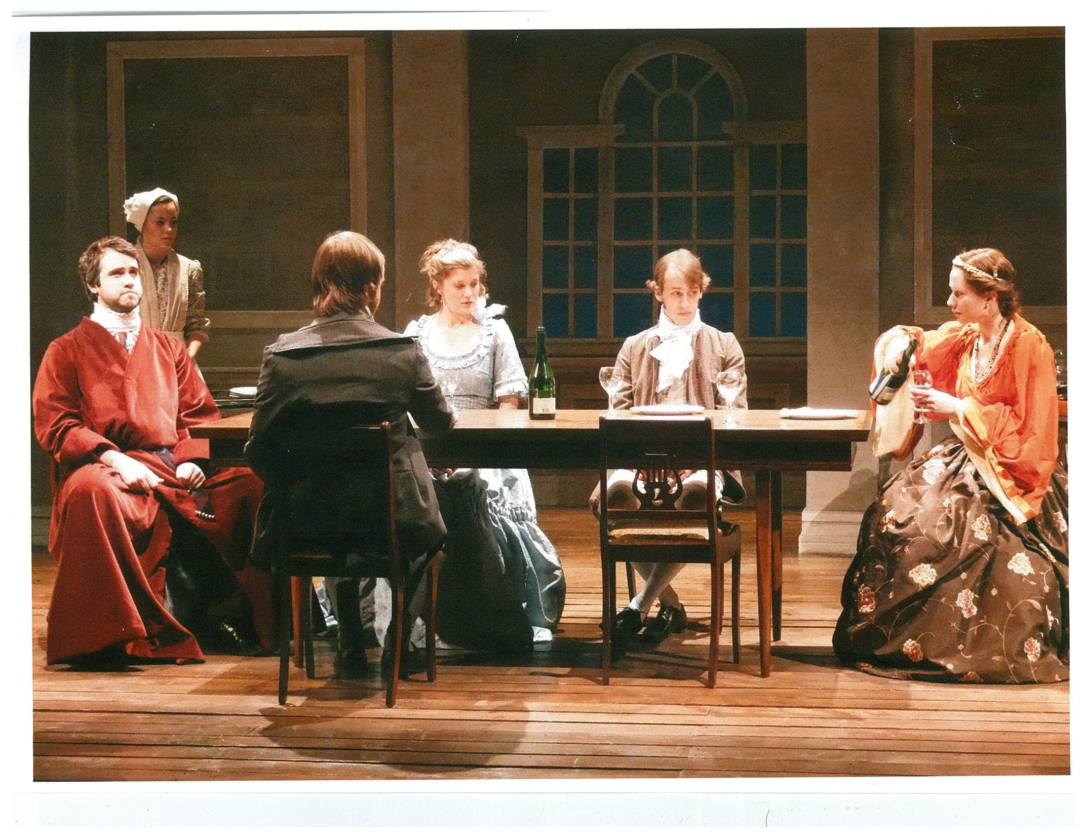 Five people sitting at a dinner table and a maid standing to the side