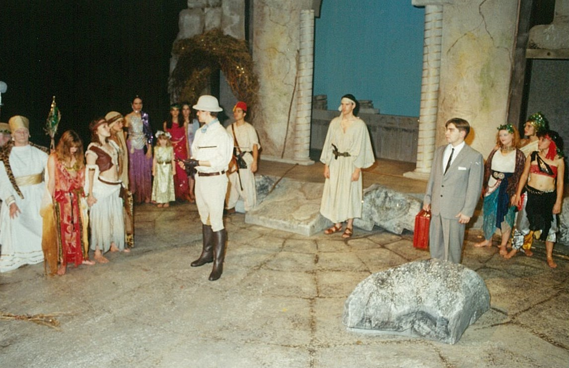 A group of people in colourful loose clothing surrounding a man in a European explorer outfit