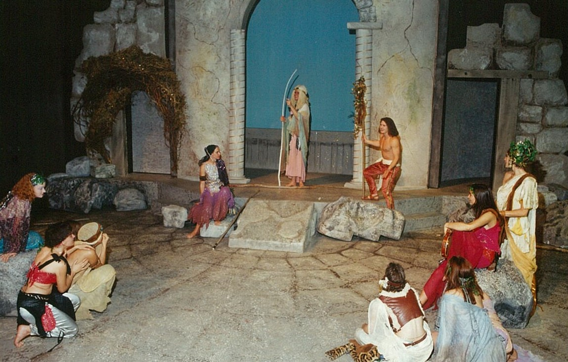 A group of people in colourful clothing gathered around a man with a white wooden staff