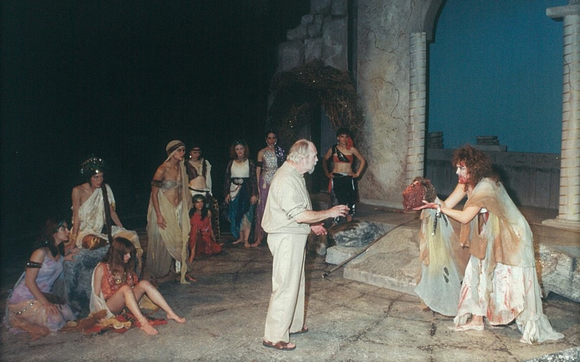 A man showing head to another man in modern clothing, a group of people surround them