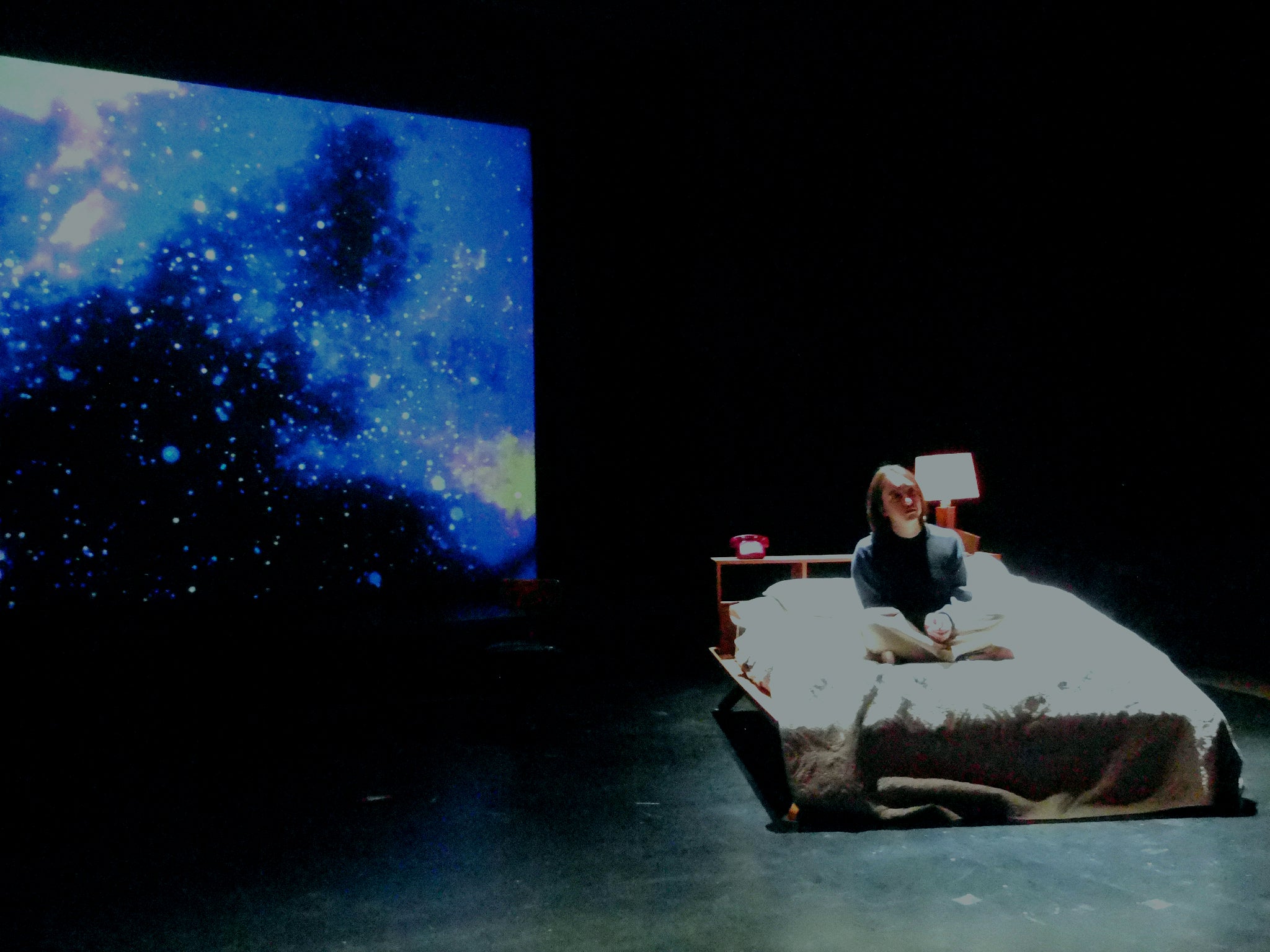 A bed is on stage and stars are projected behind