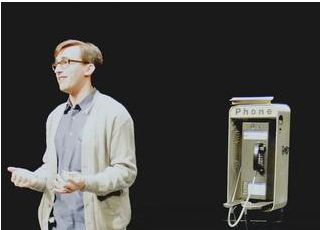 Simon stands on stage in front of a payphone