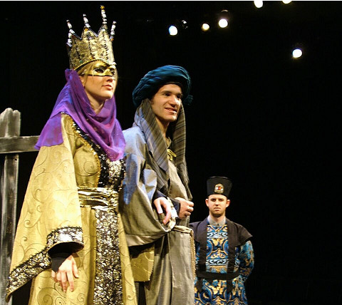 Woman standing wearing a crown with two men looking on