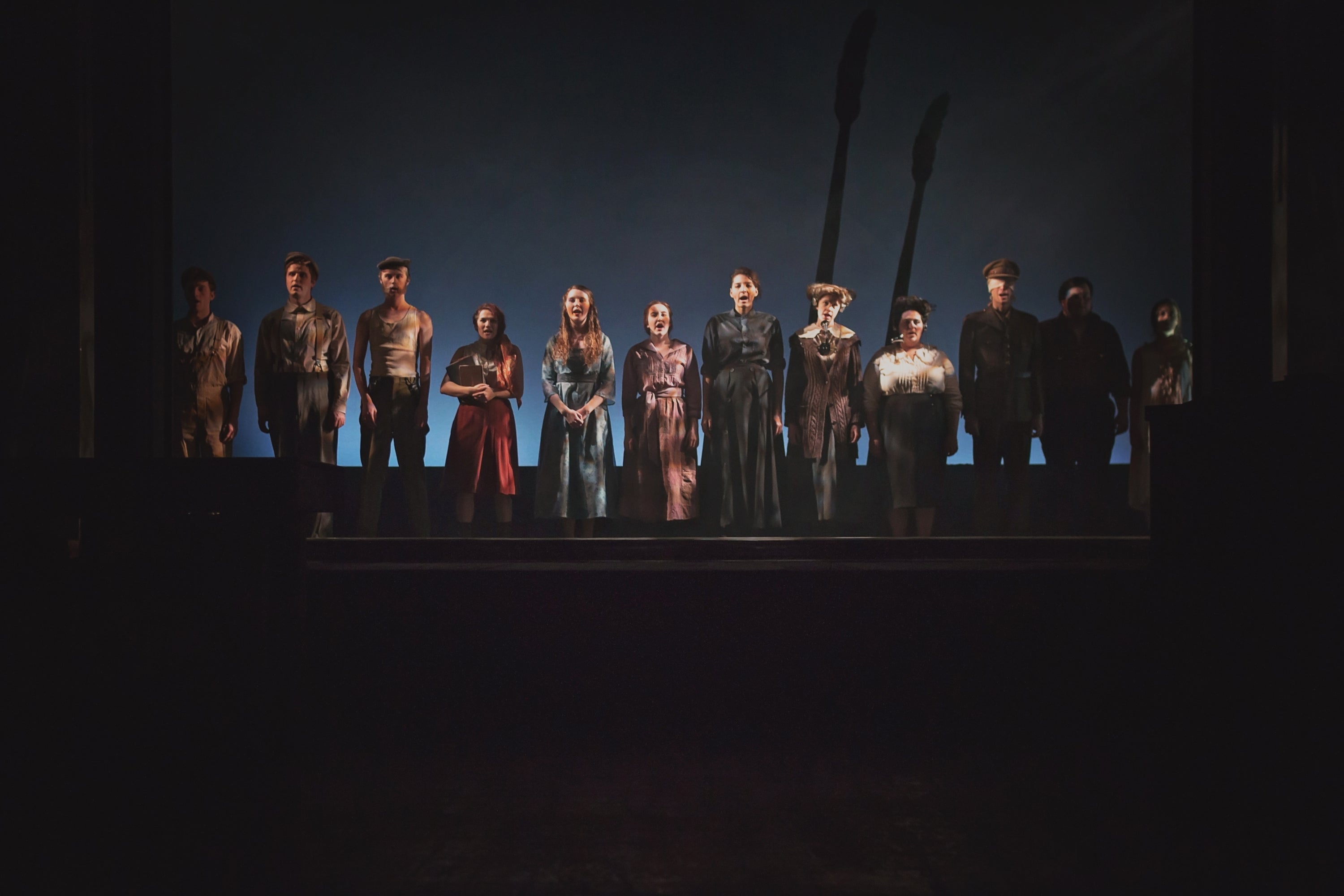 The full cast is standing on stage
