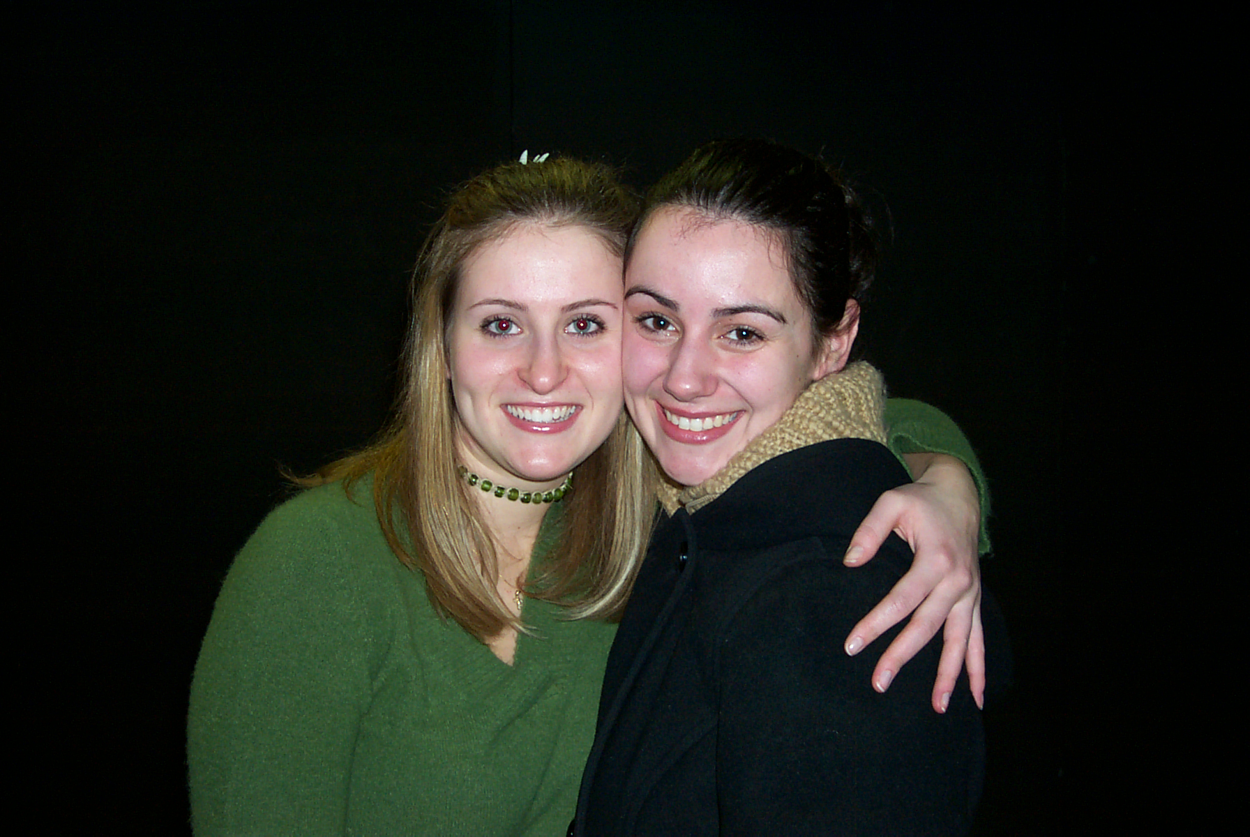 Woman in green top and woman in black top smiling and hugging