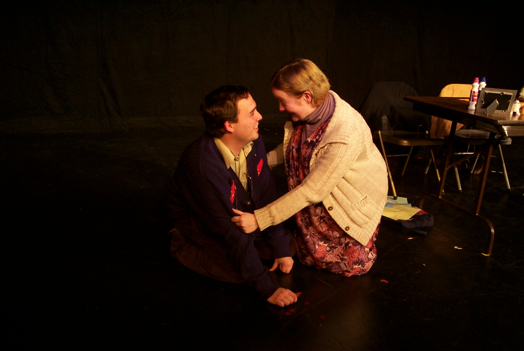 A woman in a white shawl and purple dress kneeling infront of man in blue suit