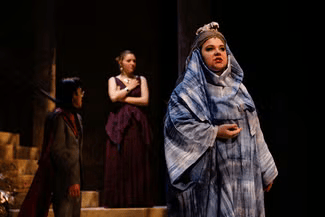 Three people on stage with different expressions, woman in front looks reflective.