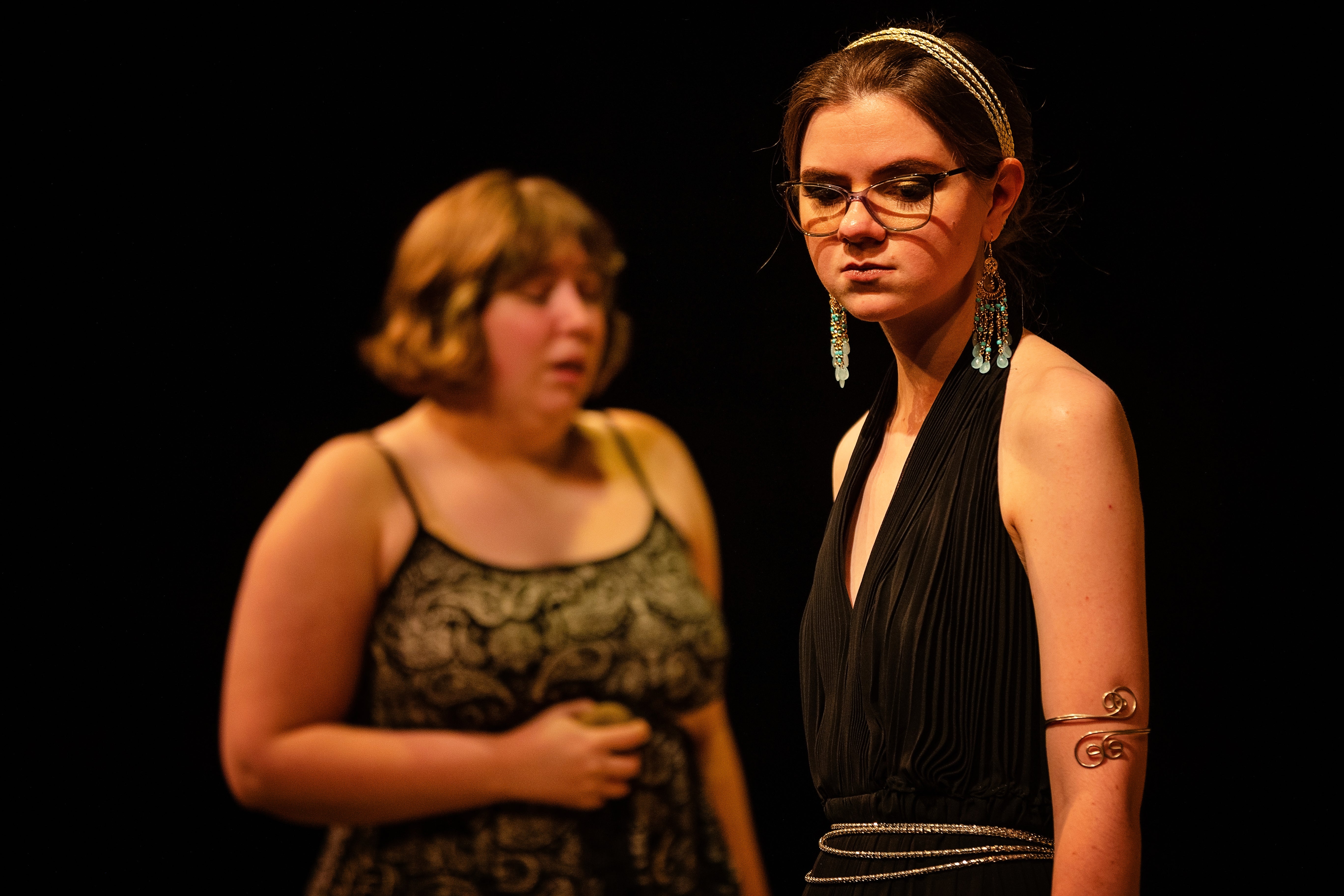 Two women onstage, one of them looks down with a sad expression