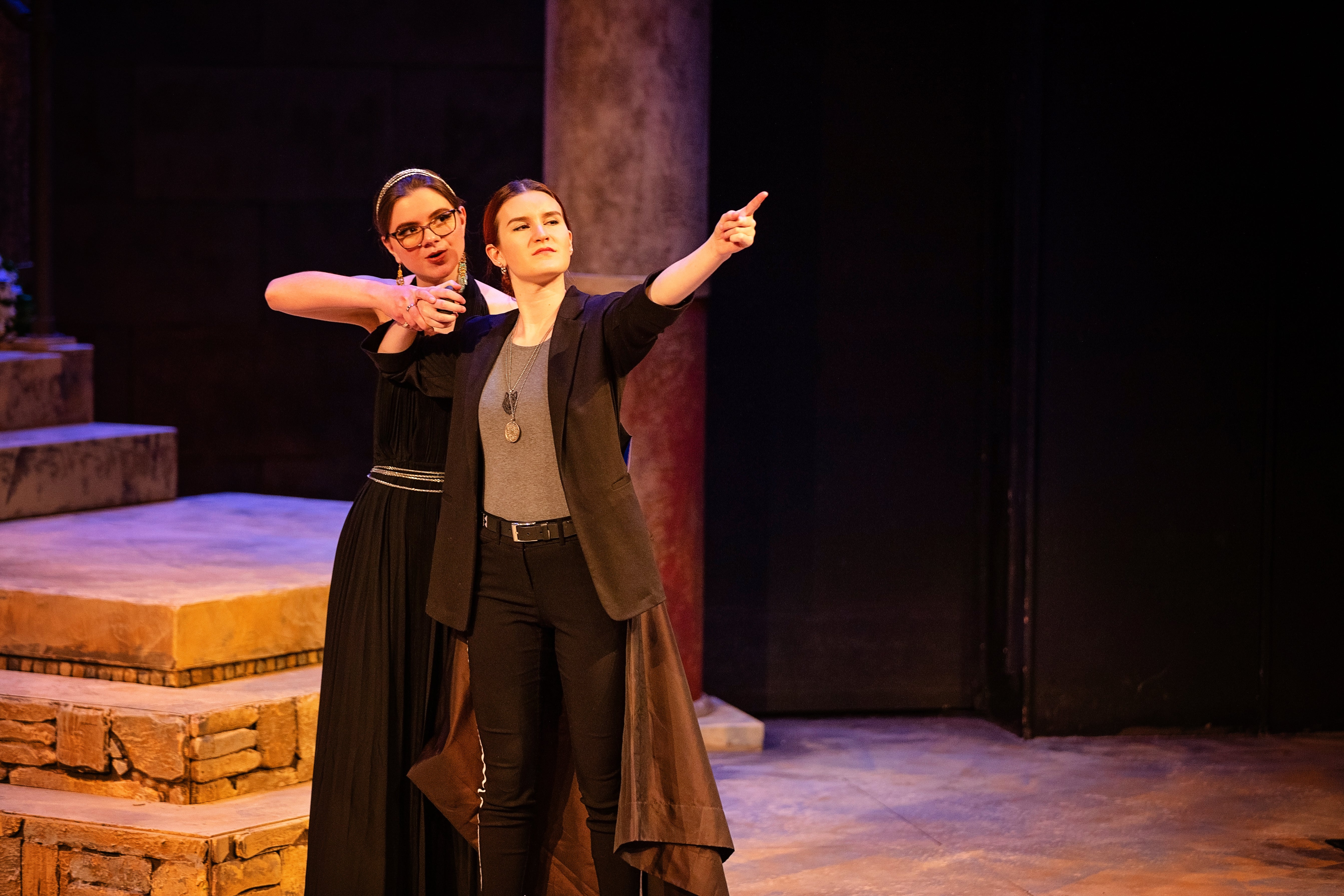 A woman points off-screen while another woman stands behind her