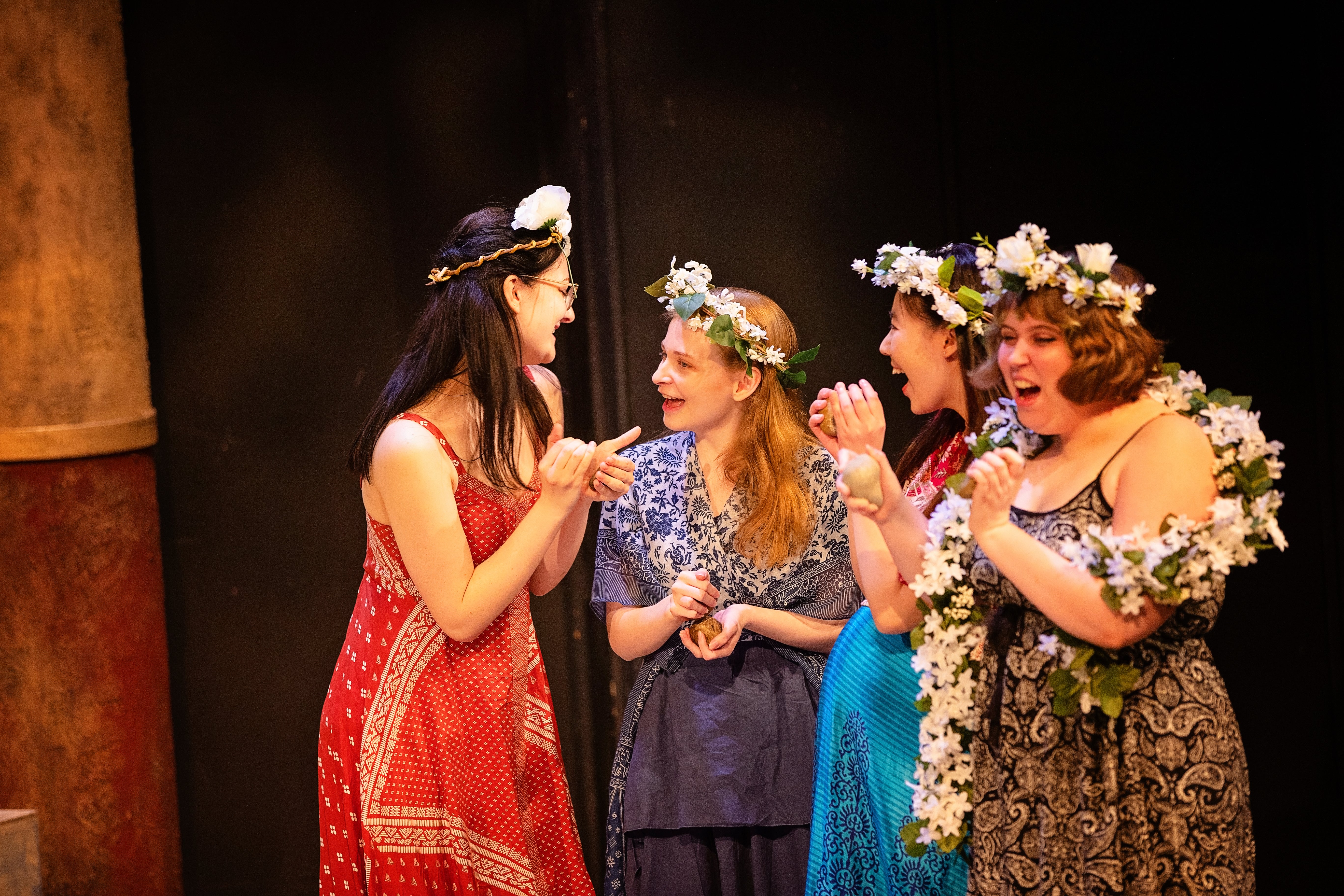 Four women wearing flower crowns, giggling and looking excited