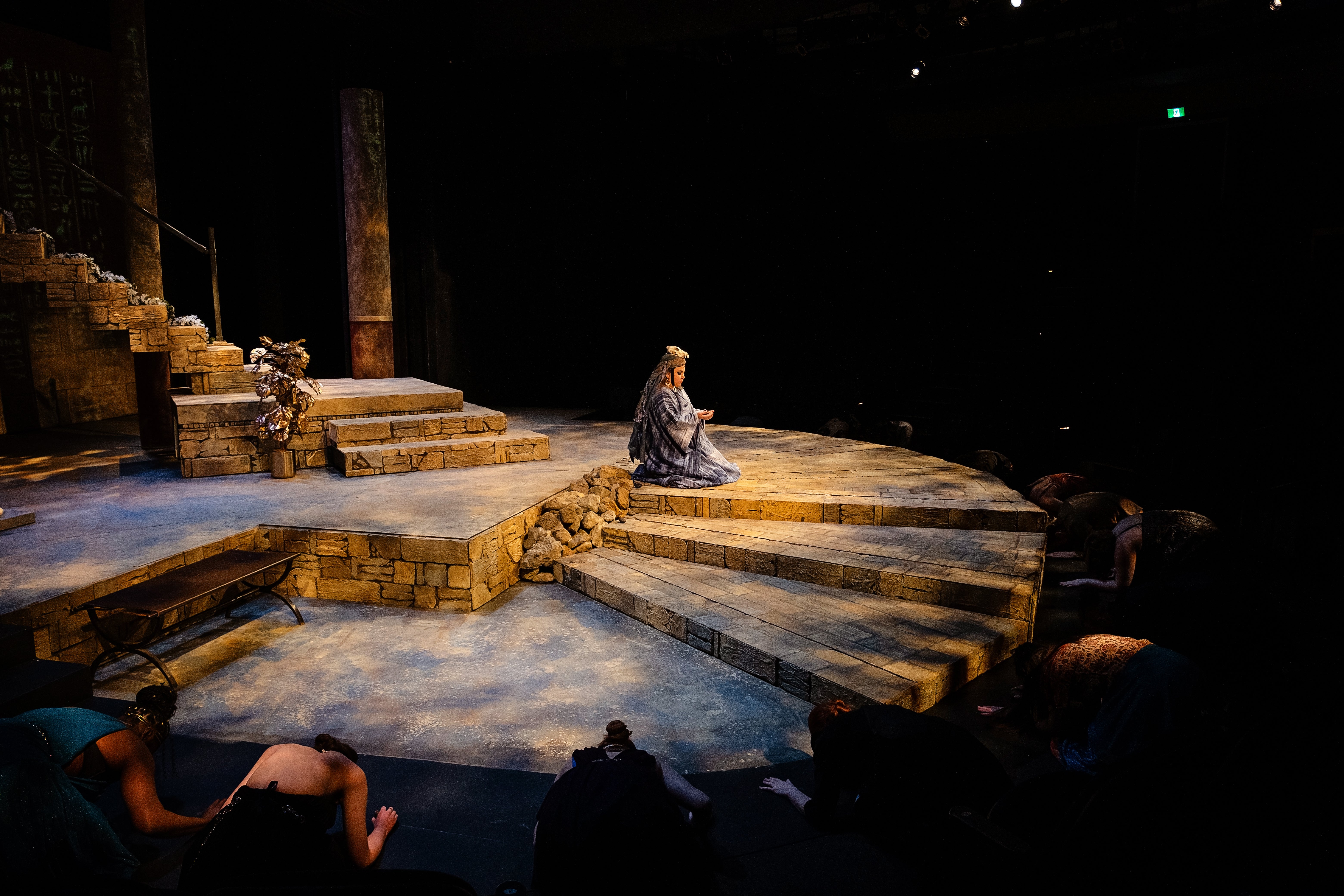 Cast kneeling in a circle around central figure on stage