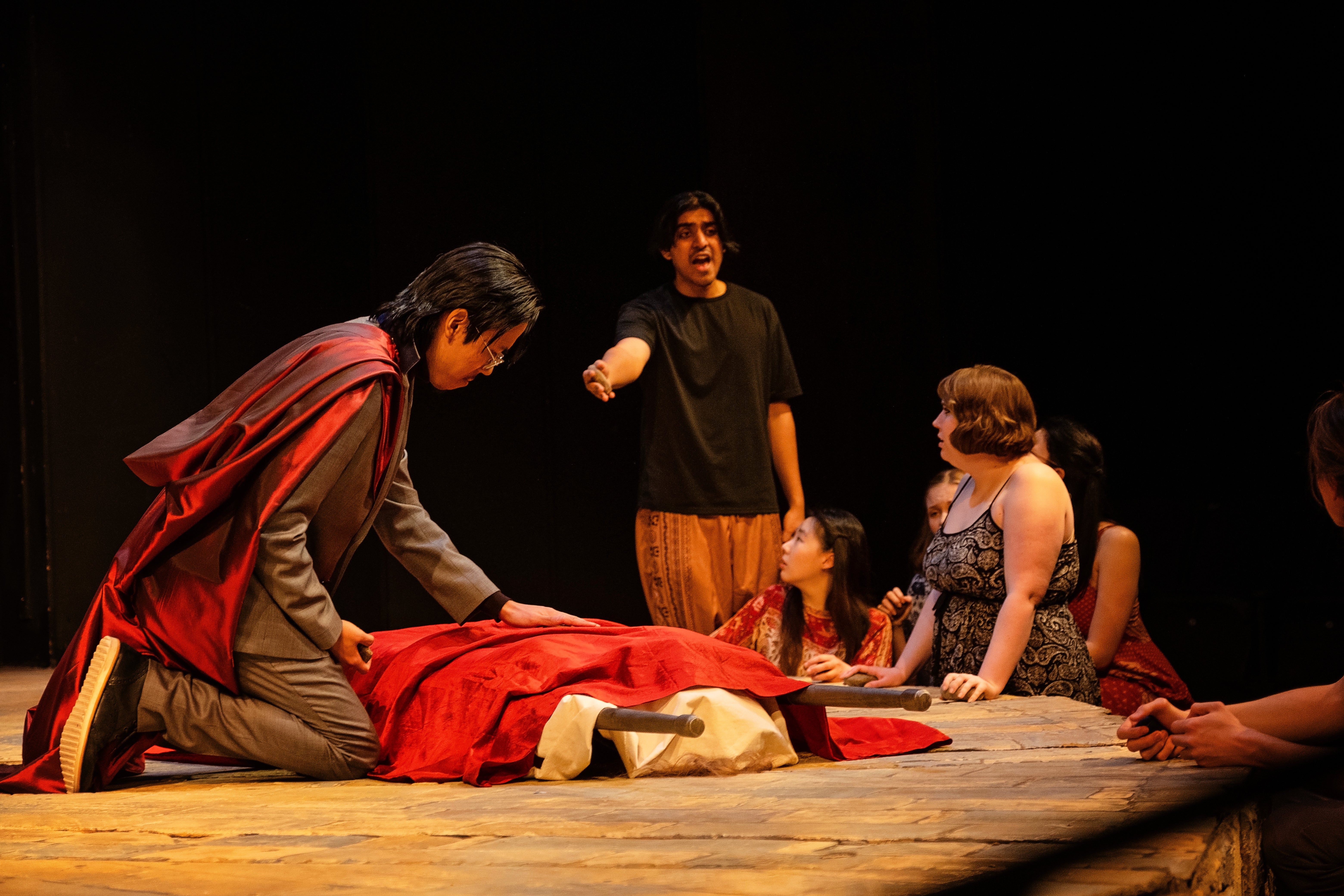 One man kneels over a body while another man yells, pointing at the body