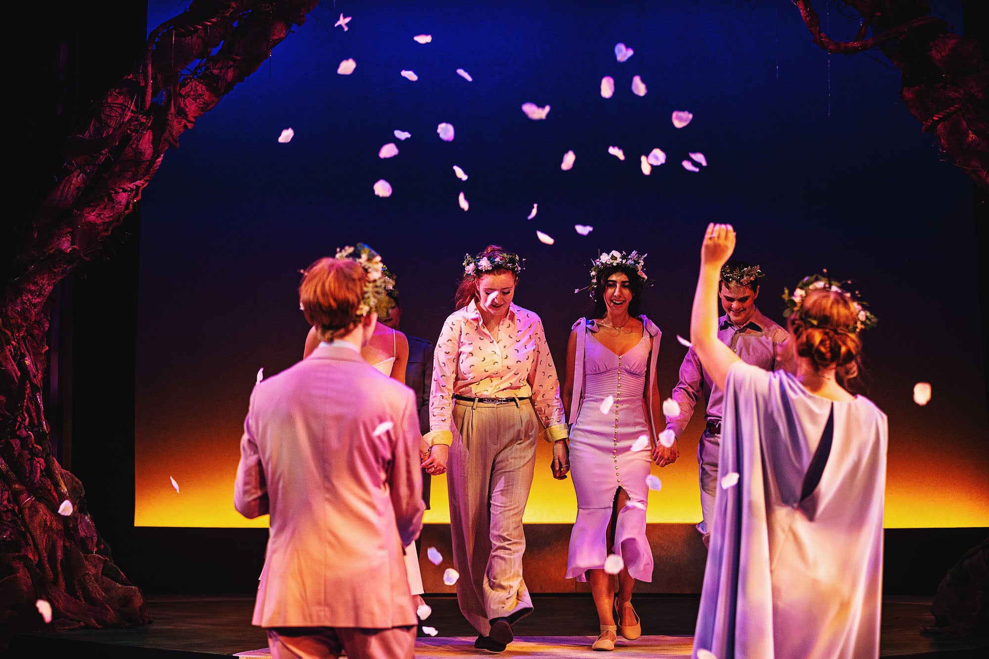 The four lovers, now joyfully wedded, walk hand in hand through a shower of flower petals and are greeted triumphantly by Theseus (Leo Ridpath) and Hippolyta (Sylvie Potje).