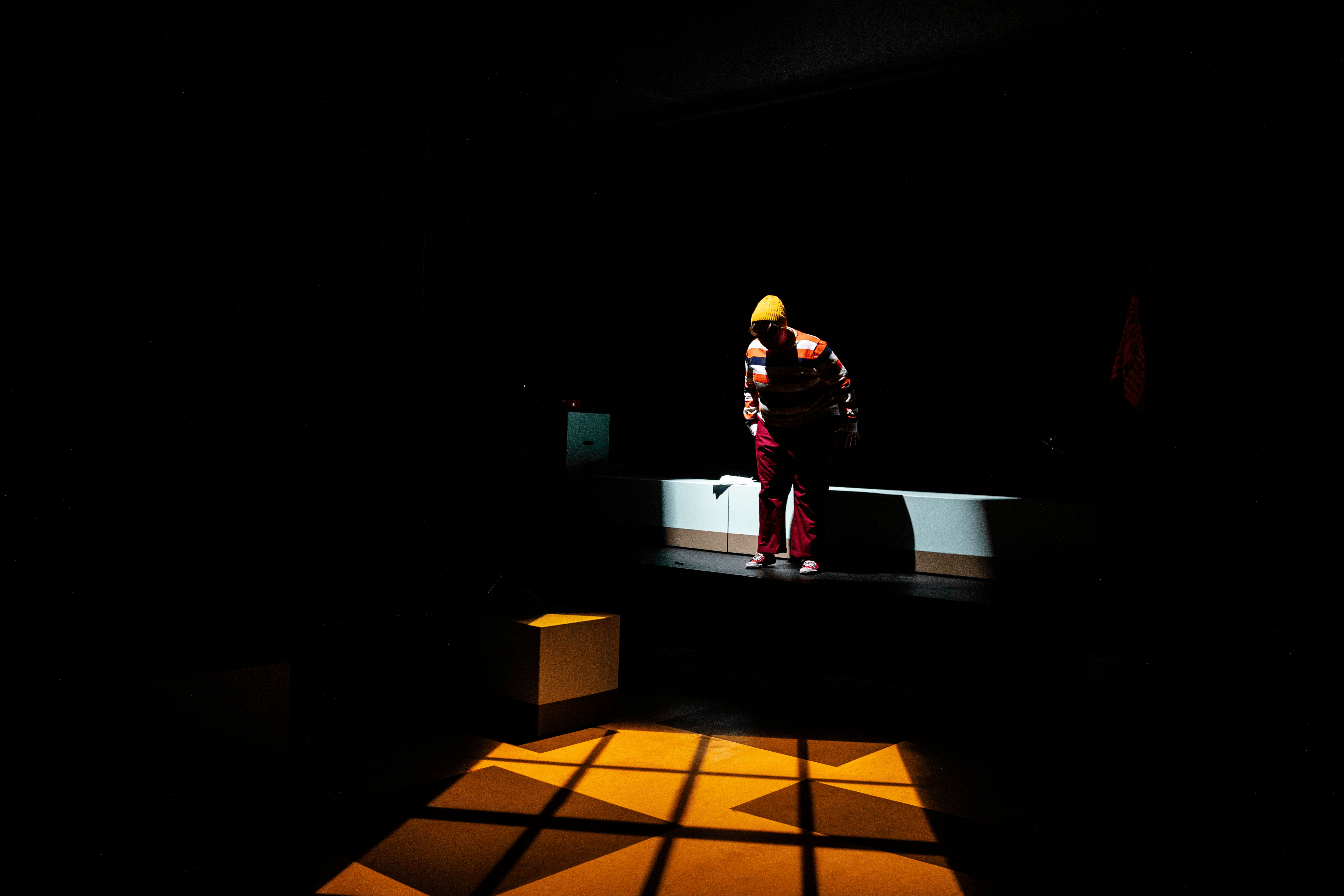 Dylan looking at the ground from a balcony with a light projection creating the reflection of a window on the ground
