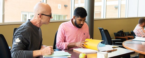 Two students collaborating and reading an open Theology textbook in class