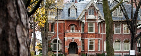 A photo of a redbrick building, in downtown toronto. There are large trees growing on the street side, with fall leaves. 