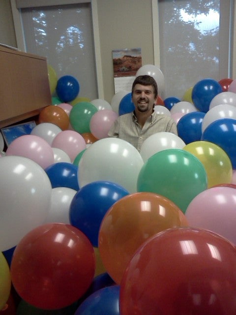 Jonathan Brubacher sits in a room full of balloons.