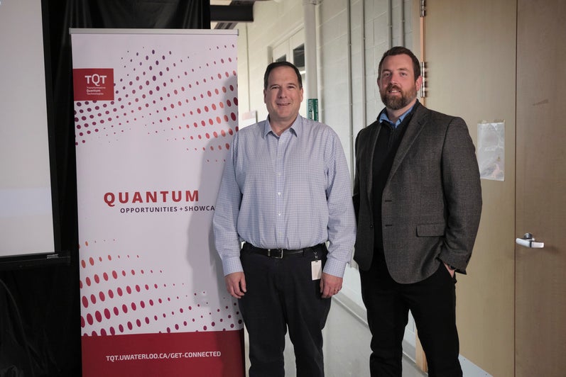 Two people standing in front of a red and white banner. 