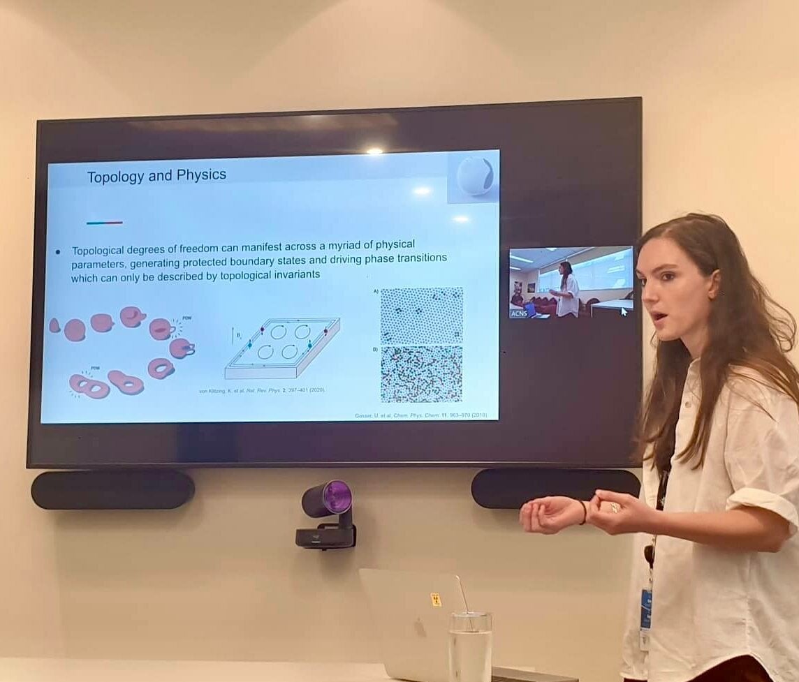 Melissa Henderson presenting infront of a TV screen. 