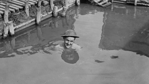 Black and white photo of man in army helmet swimming in water