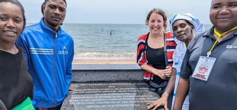 Catherine Ramey and friends by plaque by the Atlantic Ocean in Angola