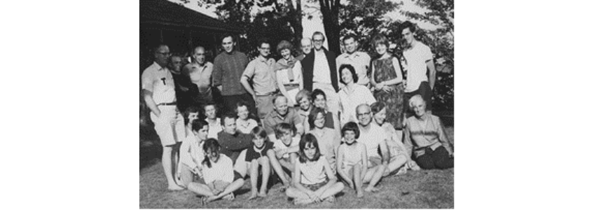 Black and White image of a group of adults and children in front of trees.