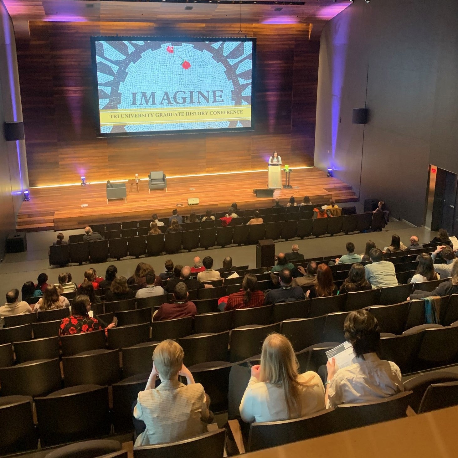 View of conference stage with "Imagine" on screen and backs of audience members