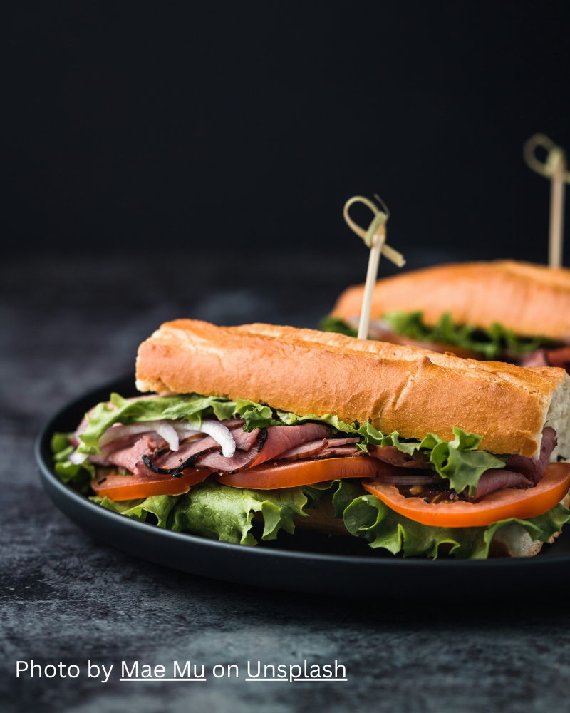 Sandwish with Brioche, lettuce, onions, tomato, sliced meat on a black plate. Text: Photo by Mae Mu on Unsplash