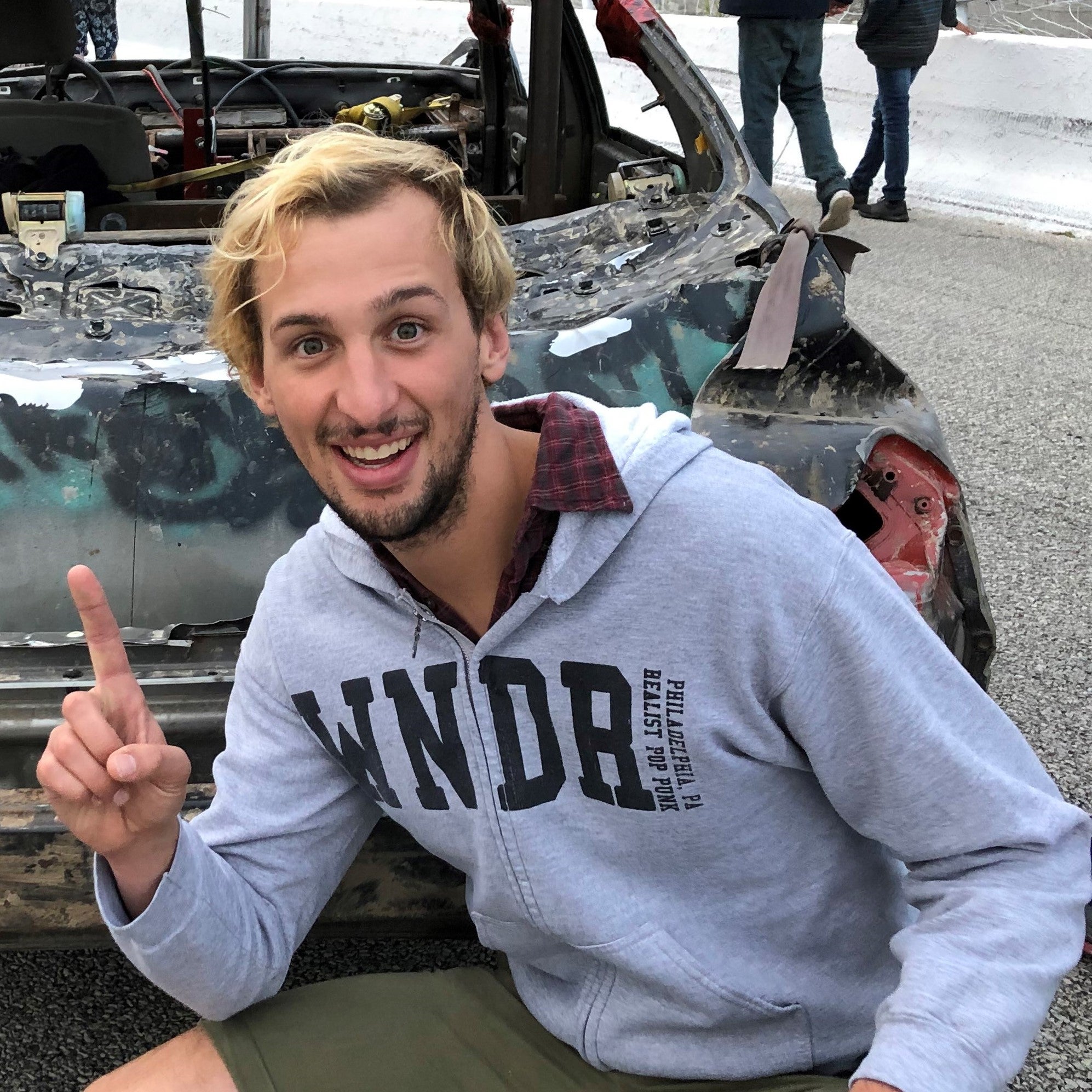 James Toenders posing in front of a wrecked car on a car track.