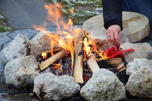 hand placing red strips of cloth into fire