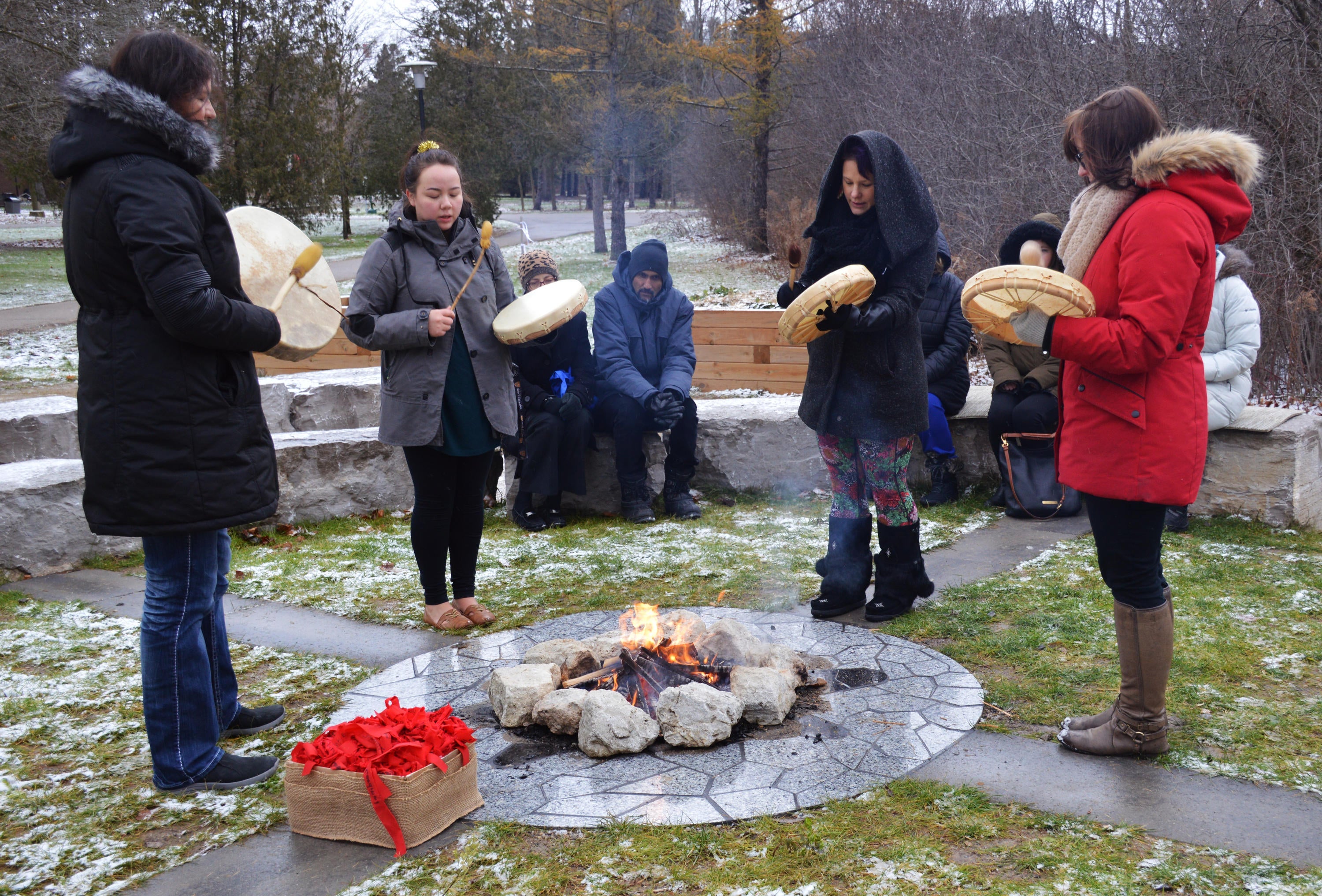 four women drumming and singing around fire