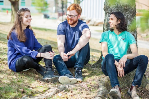 Three students sitting outside beside a tree
