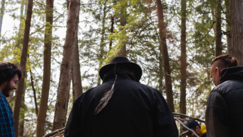 three men stand in a wooden area building a sweat lodge for ceremony