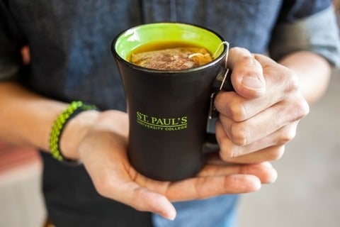 Close up of hands holding a St. Paul's mug filled with Fair Trade Tea