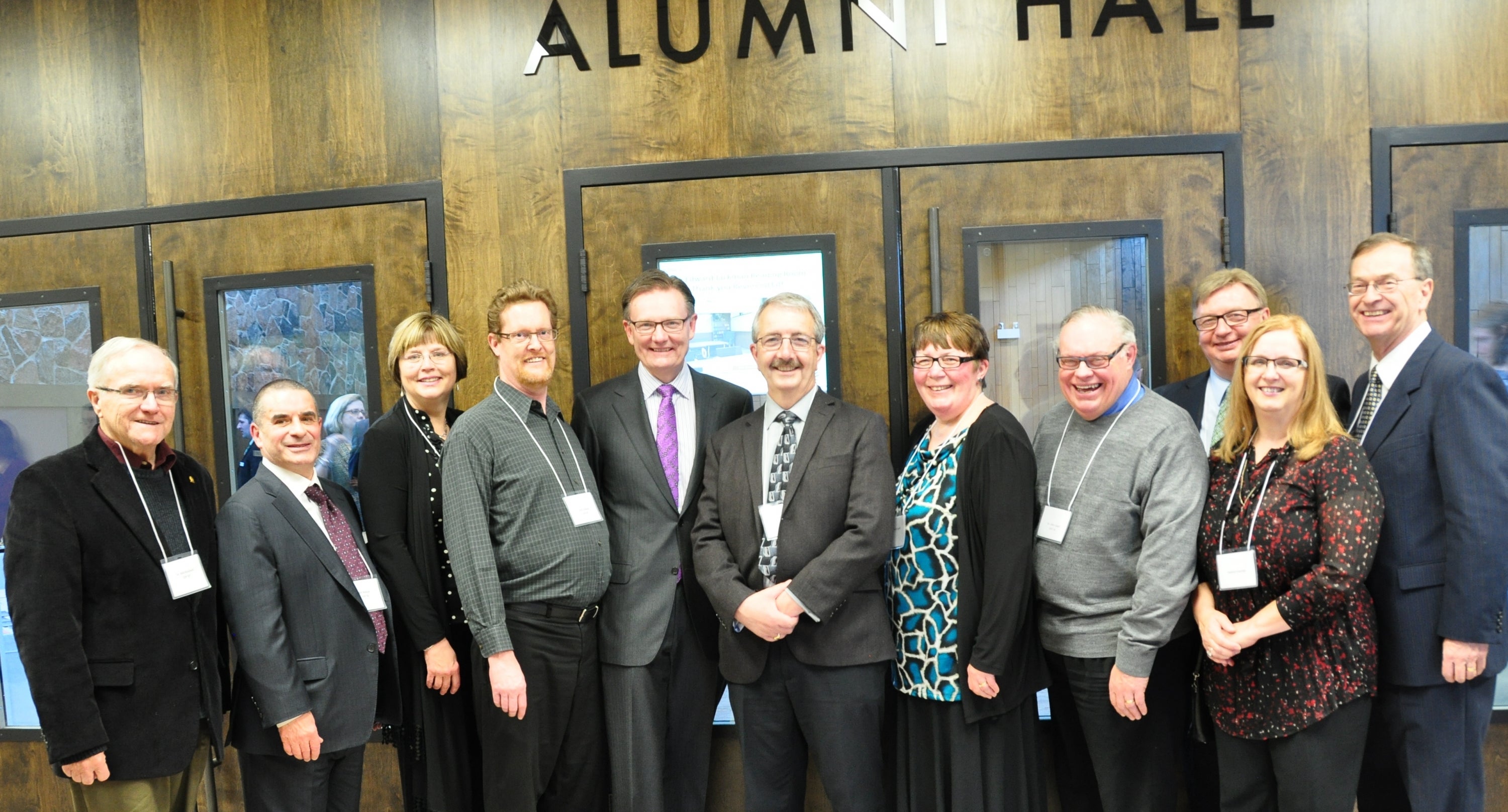 A group of alumni stand in front of the entrance to Alumni Hall