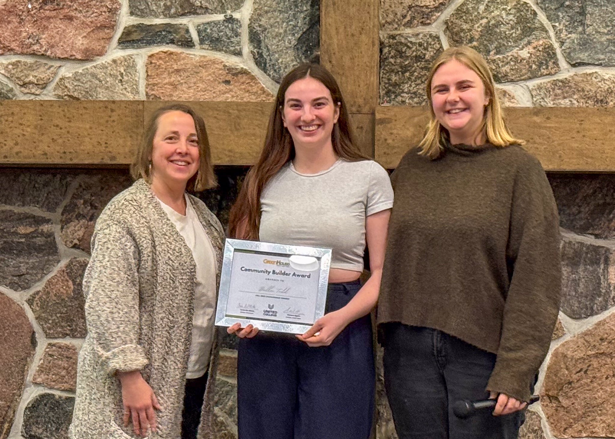Three people pose together; the person in the center holds a Community Builder Award.