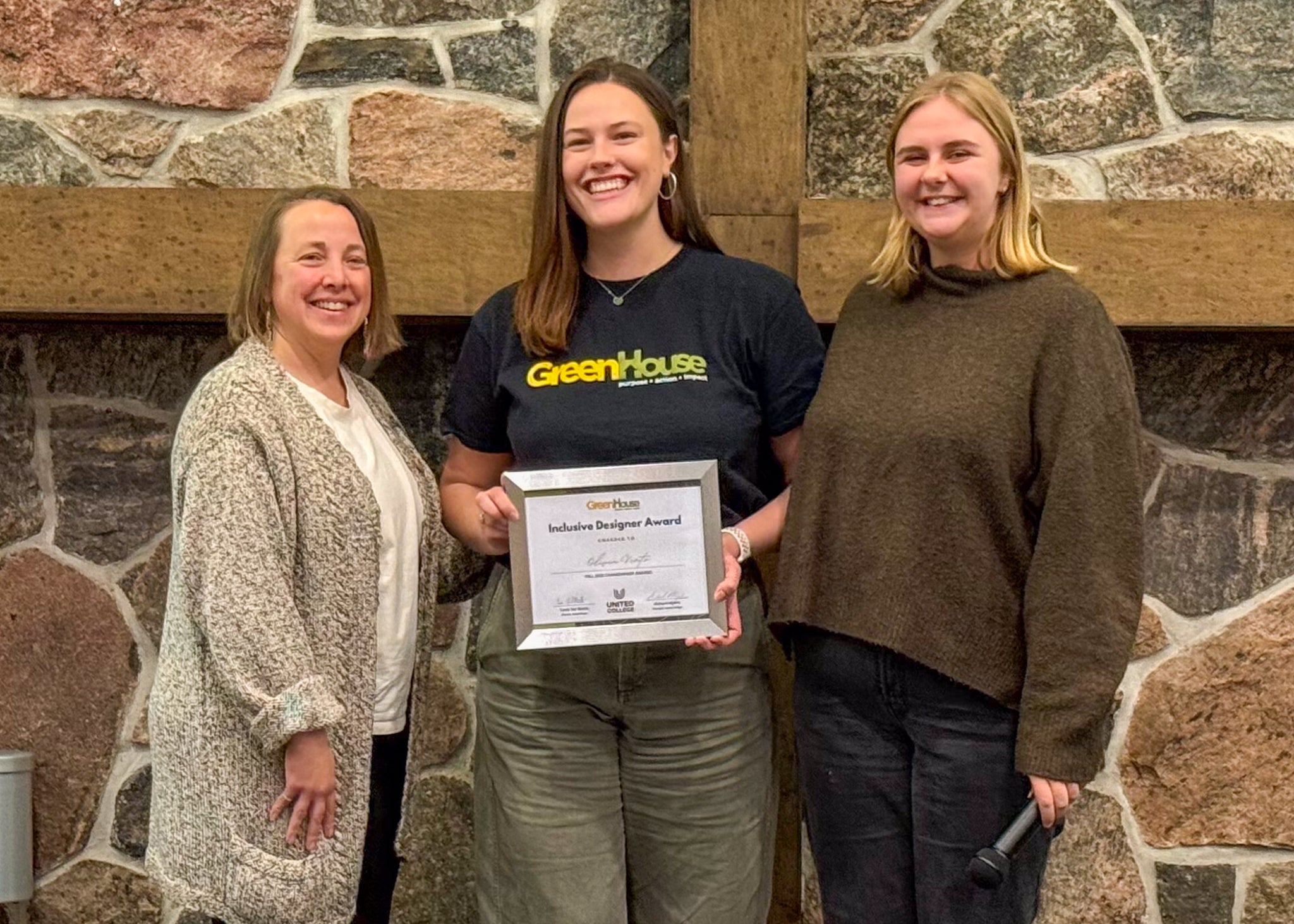 Three people stand together; the center person holds an Inclusive Designer Award.