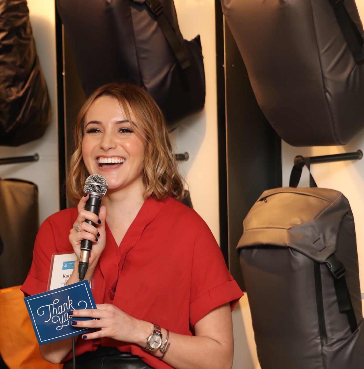Katie holding a microphone and a thank you card speaking at an event 