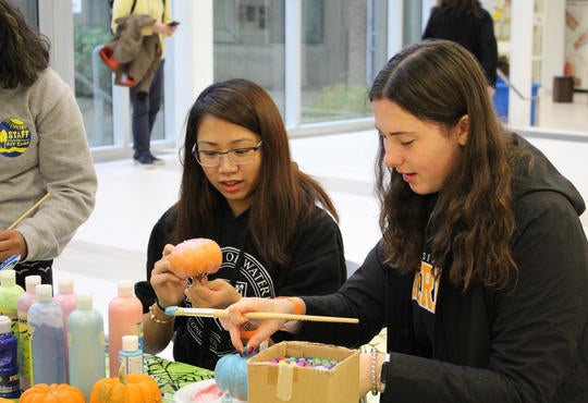 Two students paint pumpkins for a Halloween fundraiser