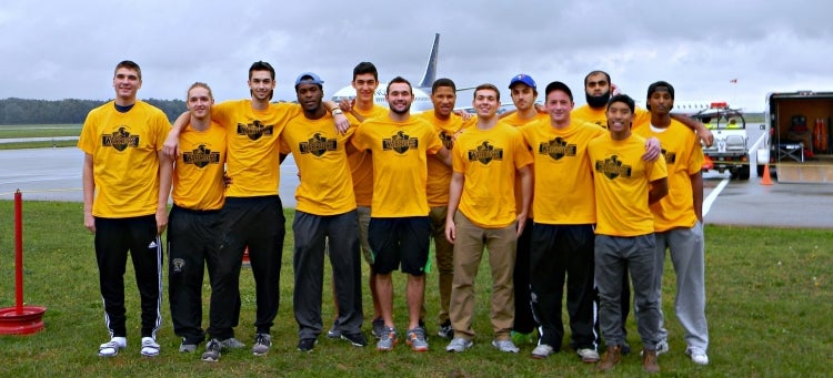 A team of student athletes stand in front of an airplane