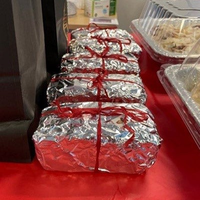 A row of loaf-shaped fruitcakes wrapped in tin foil and tied with red ribbon