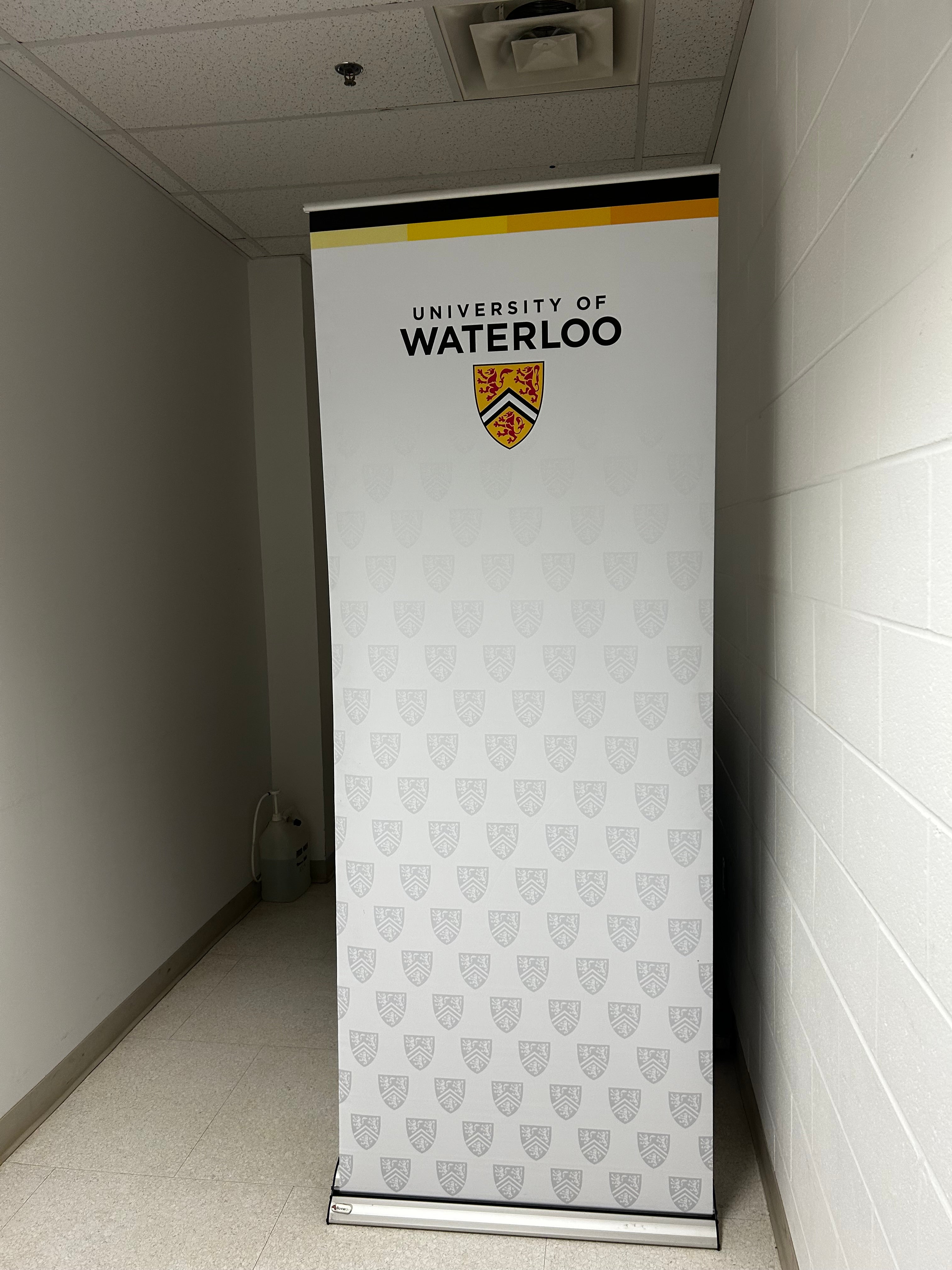 White pull up banner displaying the University of Waterloo logo with the crest at the top. 