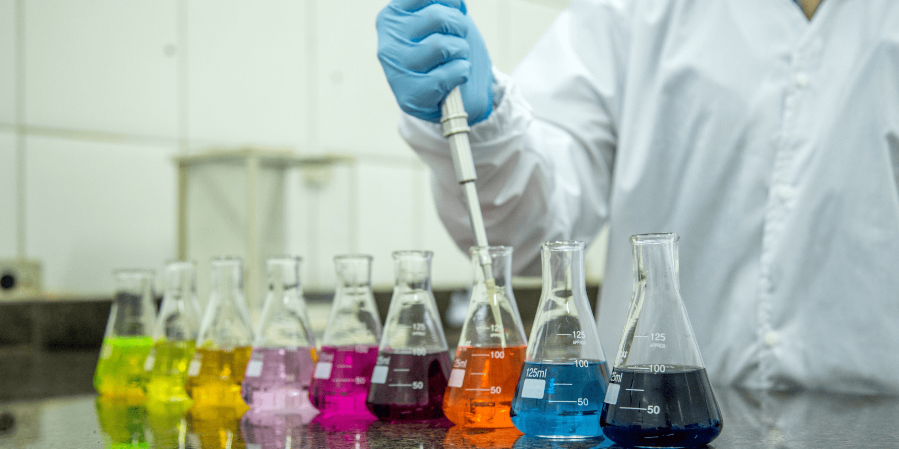 A scientist filling lab beakers with colourful solutions 