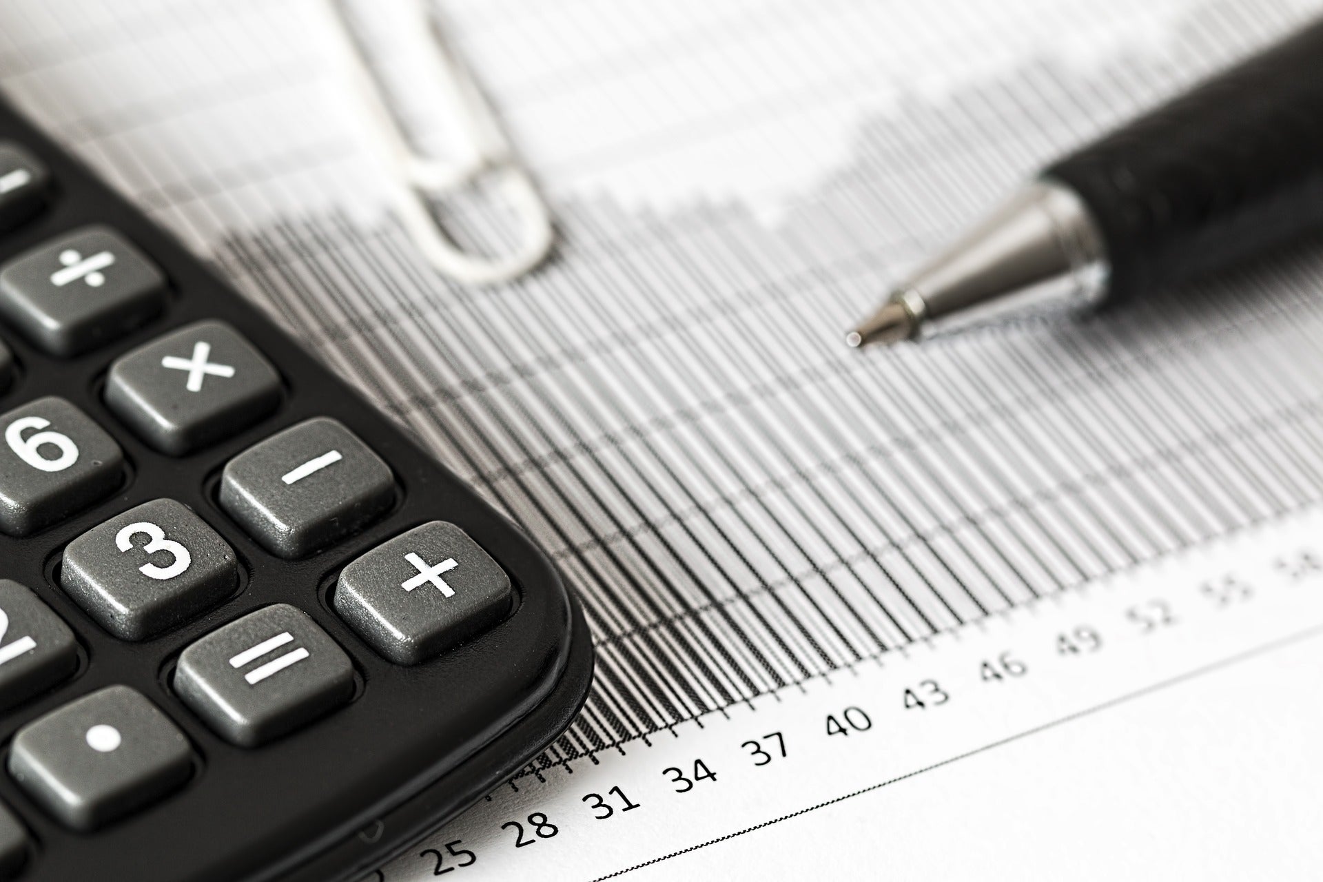 A part of a calculator is shown on the left corner of the image and a the tip of a pen is shown on the right. The two objects are on top of a paper featuring a chart.