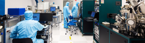 Three people wearing blue coveralls and face protection in a cleanroom