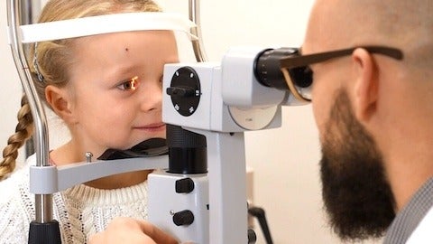 Optometrist using slit lamp to view child patient eyes