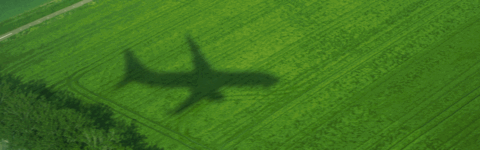Silhouette of a plane flying over green land with animated hexagons on the top right corner