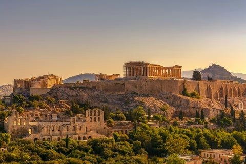 Sunset view of the Acropolis in Athens, featuring the Parthenon and surrounding ancient structures above the cityscape.